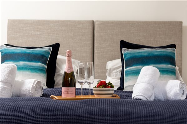 Bed with cushions, towels and tray with champaign and strawberries